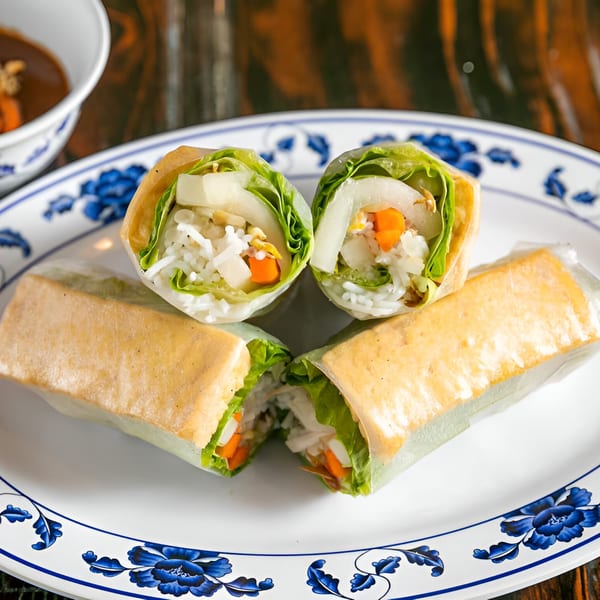 Fresh spring rolls filled with lettuce, rice noodles, carrots, and white radish on a floral plate.