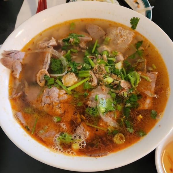 A close-up of a large bowl of Pho with beef, meatballs, and fresh herbs in a rich broth.