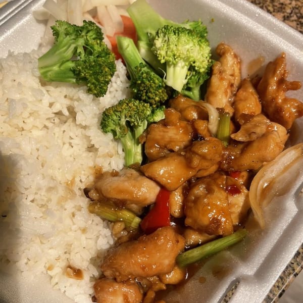 Teriyaki chicken with white rice and broccoli in a styrofoam takeout container.