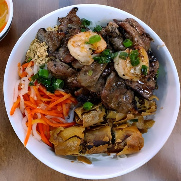 A bowl of Vietnamese vermicelli with grilled beef, shrimp, crispy spring rolls, and pickled vegetables.
