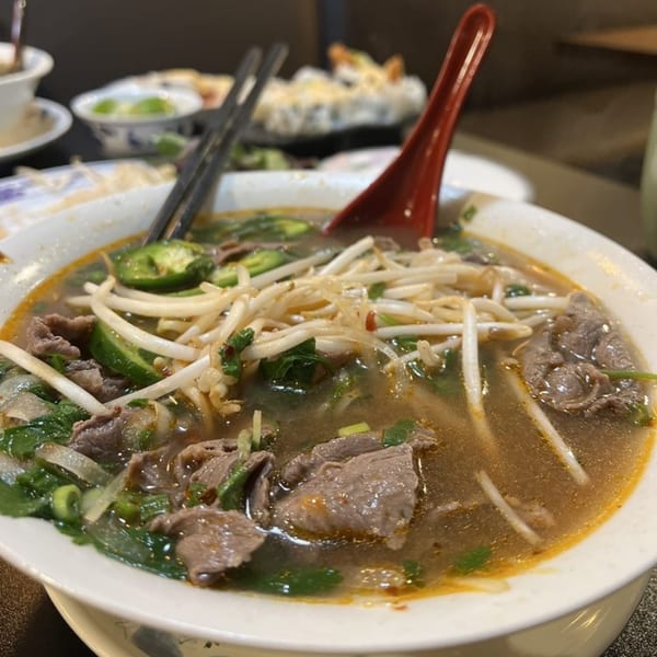 Close-up of a bowl of Pho with beef, bean sprouts, and green chilies, with a red spoon.