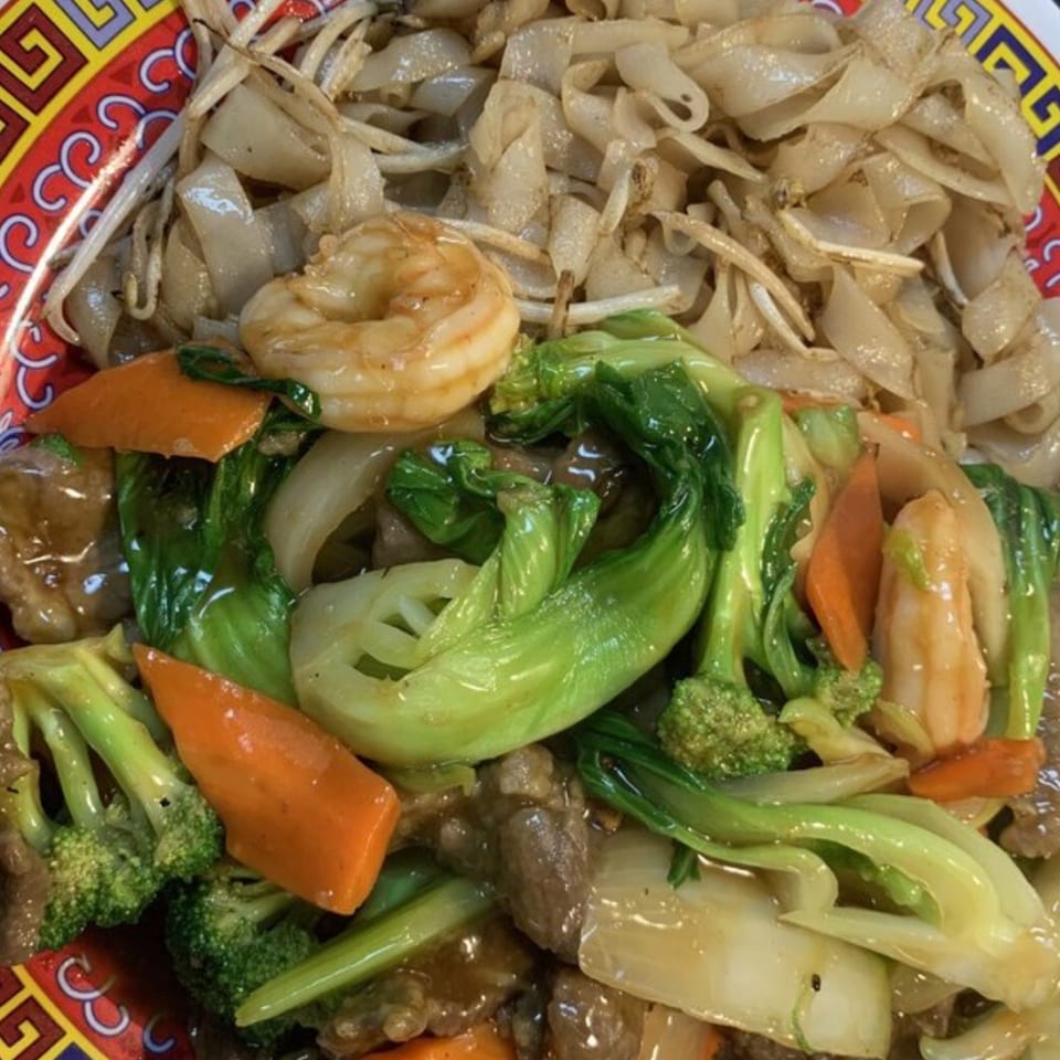 Asian fusion dish with wide noodles, shrimp, beef, broccoli, carrots, and bok choy.